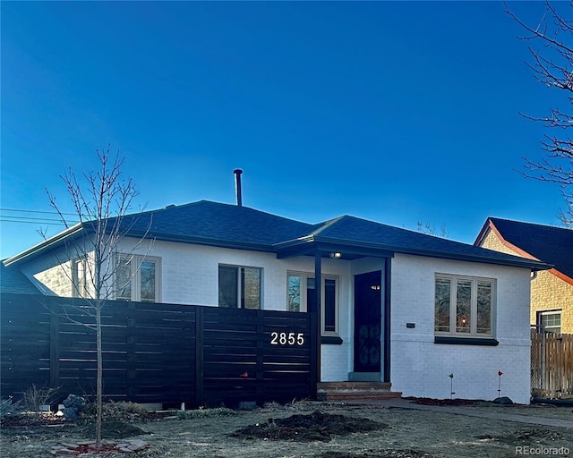 view of front of house featuring entry steps, fence, brick siding, and roof with shingles