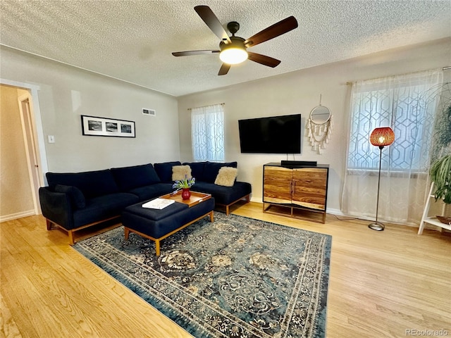 living room with a textured ceiling, wood finished floors, visible vents, and ceiling fan