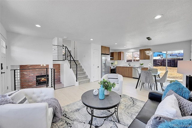 living room with a textured ceiling, a brick fireplace, and light hardwood / wood-style flooring