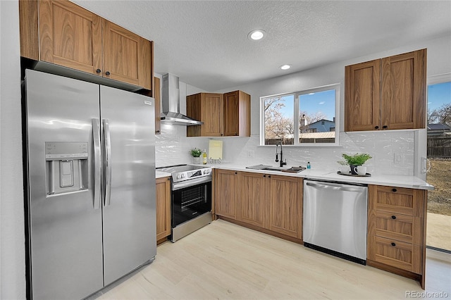 kitchen featuring sink, wall chimney range hood, stainless steel appliances, light hardwood / wood-style floors, and backsplash