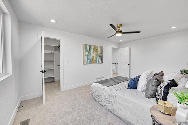 bedroom with ceiling fan, a spacious closet, light carpet, and a textured ceiling