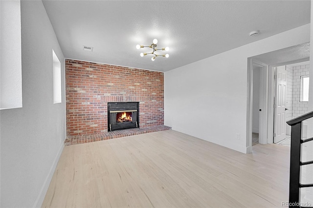 unfurnished living room with a brick fireplace, an inviting chandelier, a textured ceiling, and light hardwood / wood-style floors