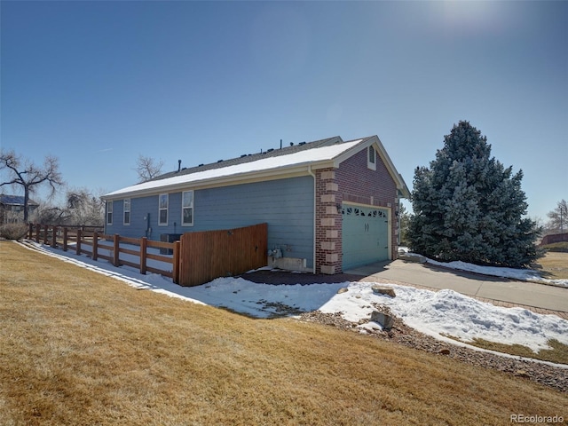 view of side of home with a garage, a yard, brick siding, and fence