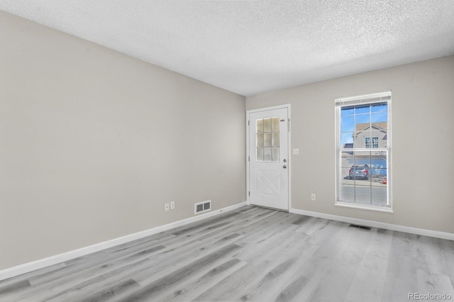 empty room featuring light wood-style floors, a textured ceiling, and baseboards