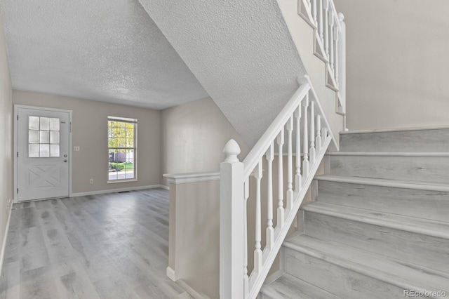 stairway with a textured ceiling, wood finished floors, and baseboards