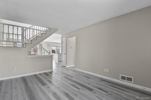 unfurnished living room with stairway, wood finished floors, baseboards, and a textured ceiling