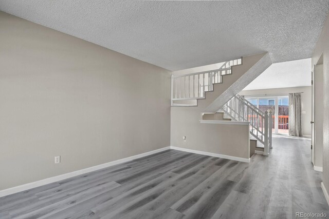 unfurnished living room featuring wood finished floors, a textured ceiling, stairway, and baseboards