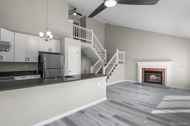 kitchen featuring ceiling fan, dark countertops, a brick fireplace, freestanding refrigerator, and high vaulted ceiling