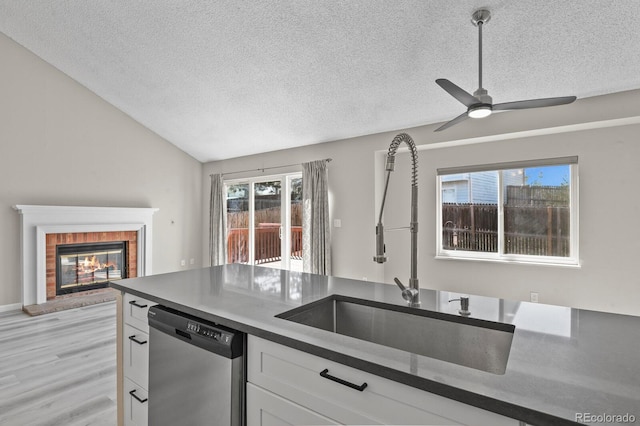 kitchen with stainless steel dishwasher, a sink, a textured ceiling, dark countertops, and vaulted ceiling