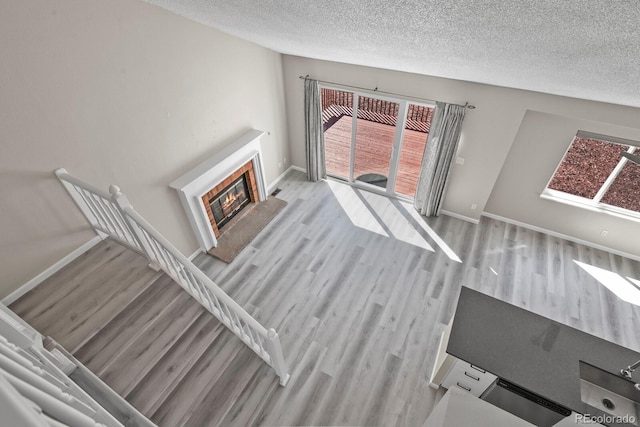 unfurnished living room with light wood-style floors, baseboards, a textured ceiling, and plenty of natural light