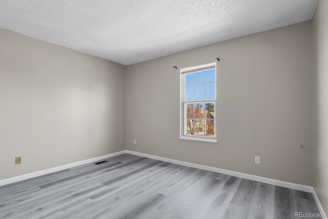 spare room featuring wood finished floors, a textured ceiling, and baseboards