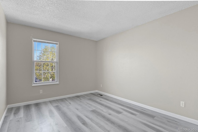 empty room with wood finished floors, a textured ceiling, and baseboards