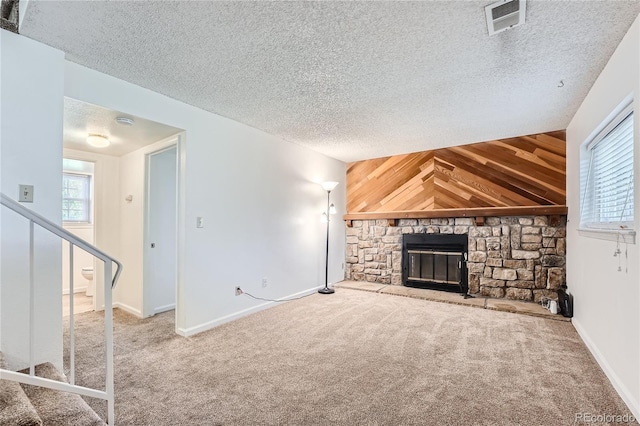 unfurnished living room with carpet, a textured ceiling, a stone fireplace, and wood walls