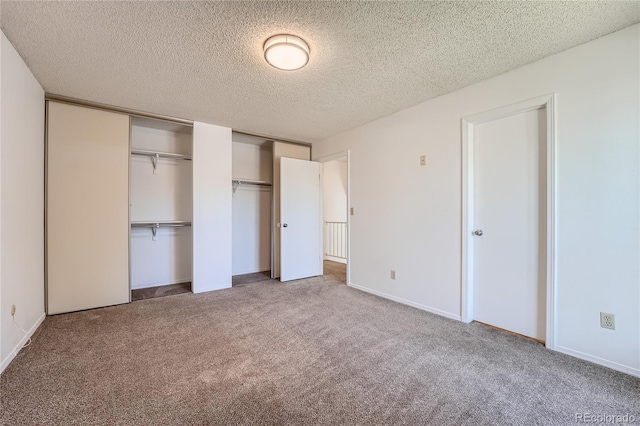 unfurnished bedroom featuring carpet flooring, a textured ceiling, and multiple closets