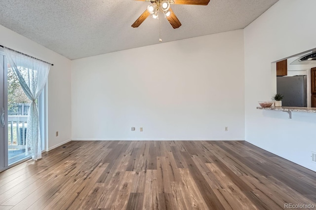 unfurnished living room featuring a textured ceiling, hardwood / wood-style flooring, vaulted ceiling, and ceiling fan