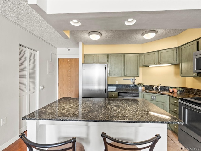 1301 Speer Blvd Unit 702, Denver, CO 80204 - kitchen with green cabinetry, stainless steel appliances, a sink, a kitchen bar, and a textured ceiling