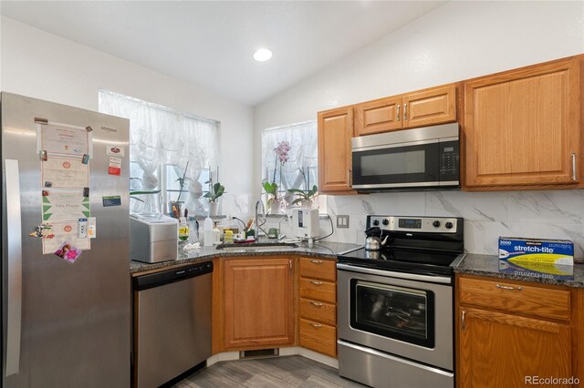 kitchen featuring stainless steel appliances, lofted ceiling, tasteful backsplash, sink, and light wood-type flooring