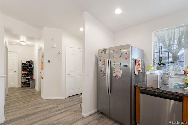 kitchen with dark stone counters, appliances with stainless steel finishes, wood-type flooring, and lofted ceiling