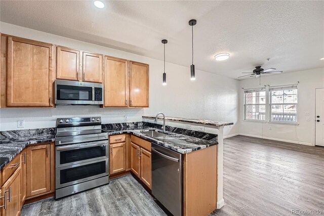 kitchen featuring sink, dark wood-type flooring, appliances with stainless steel finishes, hanging light fixtures, and dark stone counters