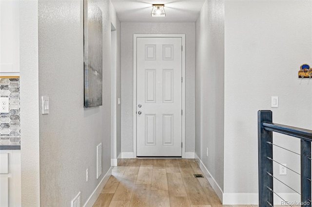 doorway with baseboards, light wood finished floors, and visible vents