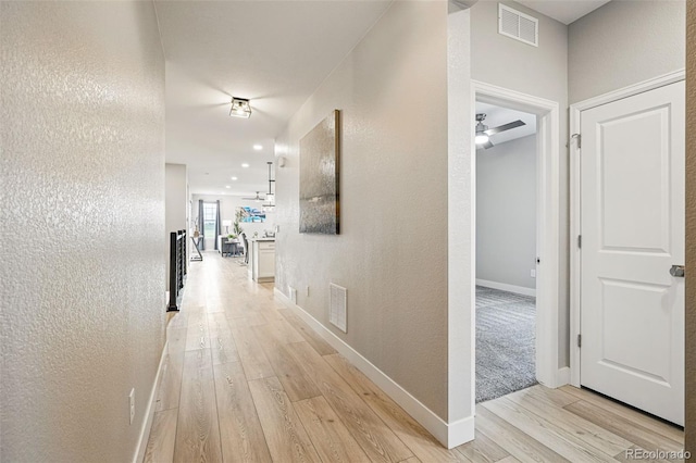 hallway featuring baseboards, visible vents, a textured wall, and light wood finished floors