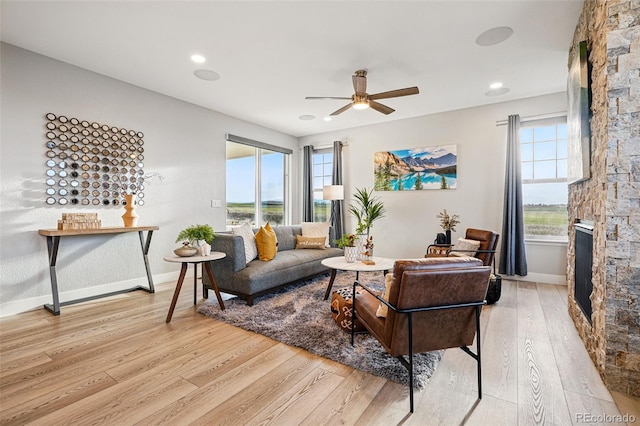 living area featuring baseboards, light wood finished floors, ceiling fan, and a healthy amount of sunlight
