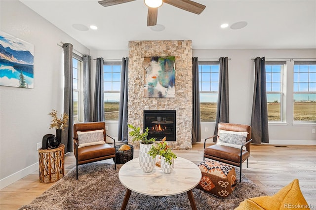 sitting room with a ceiling fan, baseboards, a stone fireplace, and light wood-style floors