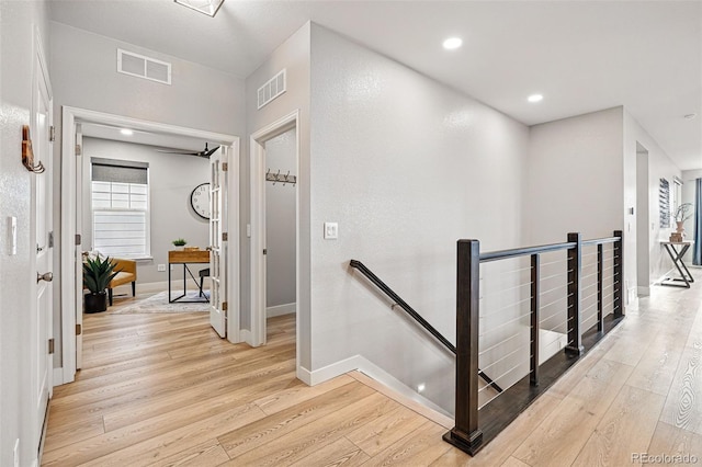 corridor with visible vents, light wood-style floors, and an upstairs landing