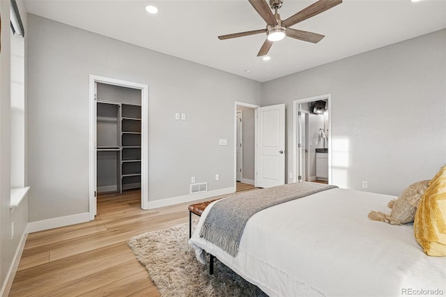 bedroom featuring baseboards, connected bathroom, light wood-style floors, a spacious closet, and recessed lighting