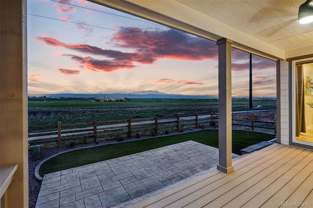 deck at dusk featuring a lawn, fence, a patio, and a rural view