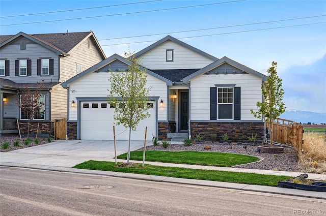 view of front facade with driveway, roof with shingles, fence, an attached garage, and stone siding