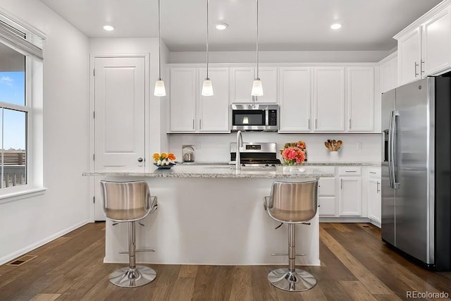 kitchen with appliances with stainless steel finishes, white cabinets, decorative light fixtures, and a center island with sink