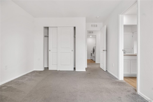 unfurnished bedroom featuring a closet, connected bathroom, separate washer and dryer, and light colored carpet