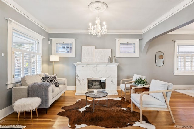 living area featuring ornamental molding, a premium fireplace, light hardwood / wood-style floors, and a notable chandelier