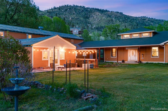 back house at dusk featuring a mountain view, a patio area, and a lawn