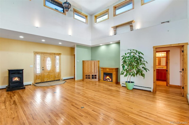 living room with baseboard heating, a towering ceiling, a fireplace, and light hardwood / wood-style floors