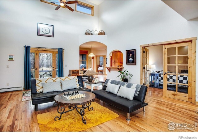 living room featuring ceiling fan, a towering ceiling, light wood-type flooring, and baseboard heating