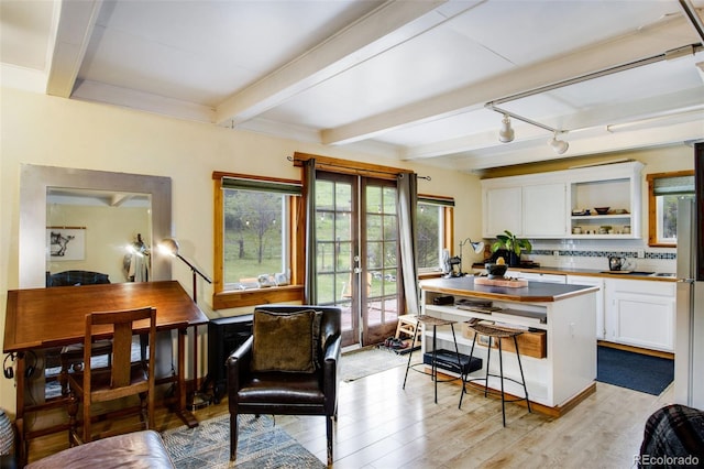 interior space with beamed ceiling, white cabinets, decorative backsplash, light hardwood / wood-style floors, and french doors