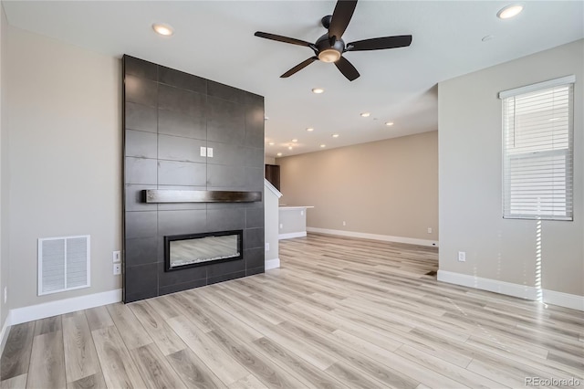 unfurnished living room featuring a tile fireplace, ceiling fan, and light wood-type flooring