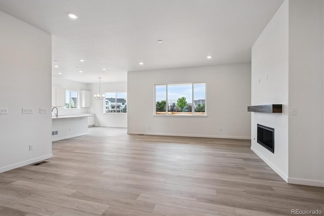 9197 Ironwood St, Highlands Ranch, CO 80129 - unfurnished living room featuring a glass covered fireplace, a chandelier, light wood-style floors, and recessed lighting