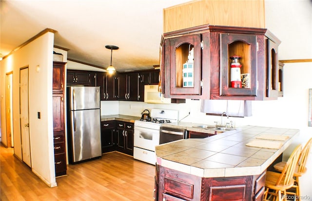 kitchen featuring tile counters, stainless steel appliances, sink, pendant lighting, and light wood-type flooring