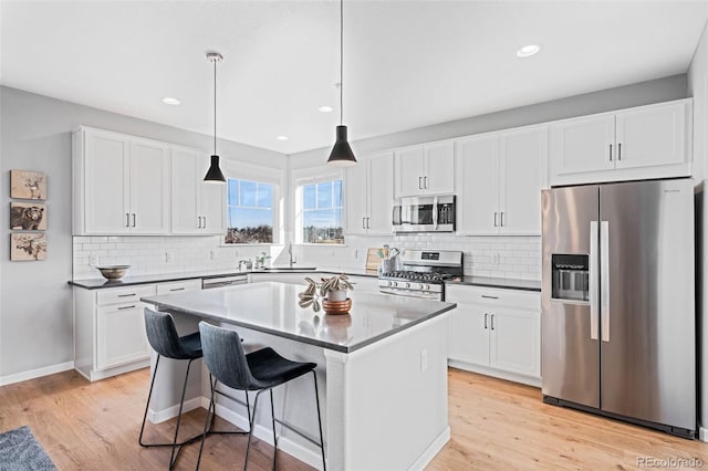 kitchen with a breakfast bar area, stainless steel appliances, a center island, pendant lighting, and white cabinets