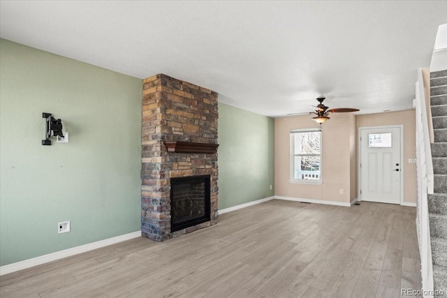 unfurnished living room featuring stairs, baseboards, a fireplace, and wood finished floors