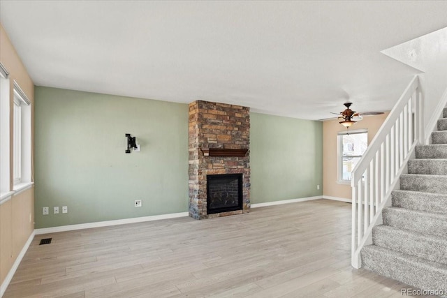 unfurnished living room with a stone fireplace, wood finished floors, visible vents, baseboards, and stairway