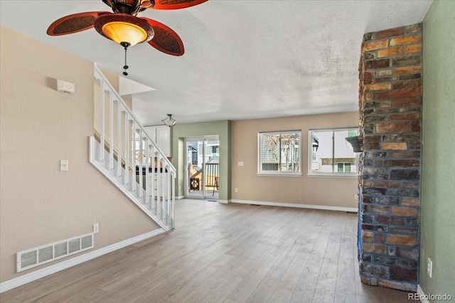 unfurnished living room featuring baseboards, visible vents, wood finished floors, stairs, and a textured ceiling