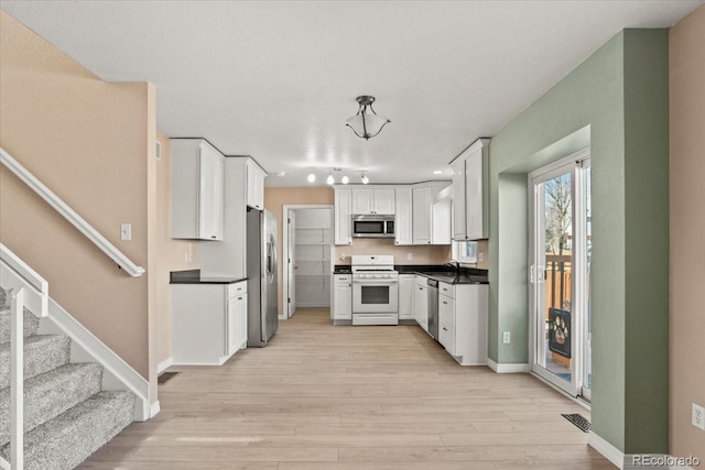 kitchen featuring dark countertops, light wood-style flooring, appliances with stainless steel finishes, white cabinetry, and a sink