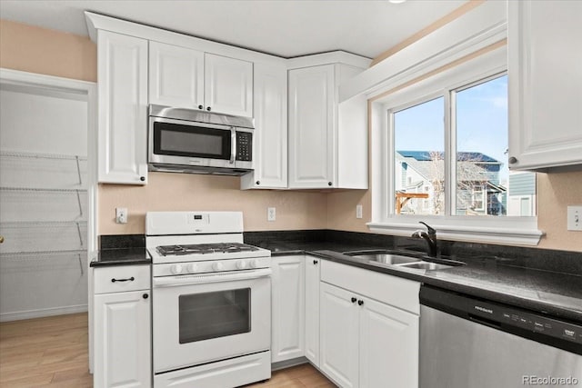 kitchen with stainless steel appliances, dark countertops, white cabinetry, and a sink