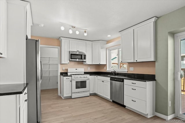 kitchen with appliances with stainless steel finishes, dark countertops, a sink, and white cabinetry