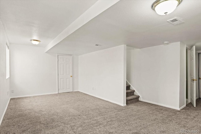 finished below grade area featuring visible vents, stairway, carpet flooring, a textured ceiling, and baseboards