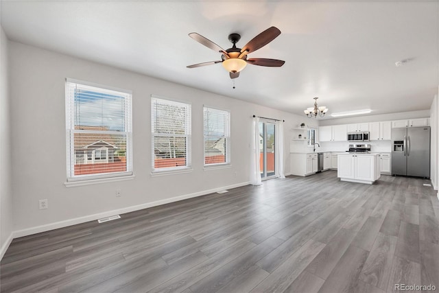 unfurnished living room featuring visible vents, a healthy amount of sunlight, ceiling fan with notable chandelier, and wood finished floors